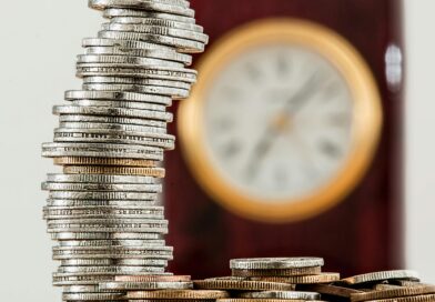 A close-up image of stacked coins with a blurred clock, symbolizing time and money relationship.